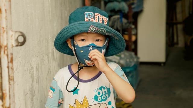 Young boy indoors wearing a hat and mask, embracing modern urban style.