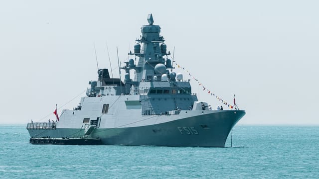 A naval warship with identification F515 sails on calm turquoise waters under a clear sky.