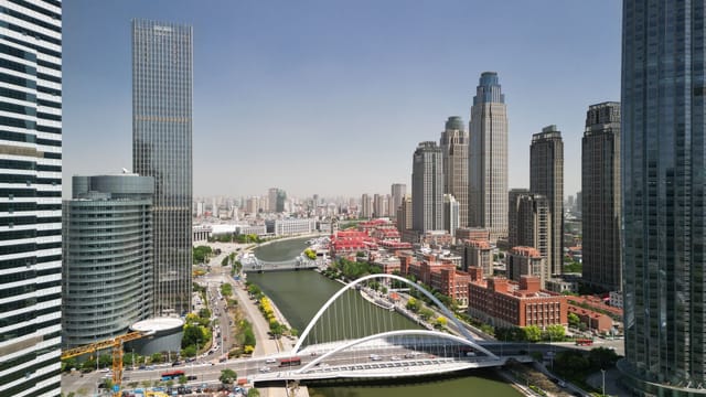 Aerial view of Tianjin city skyline featuring modern skyscrapers and distinctive bridge.
