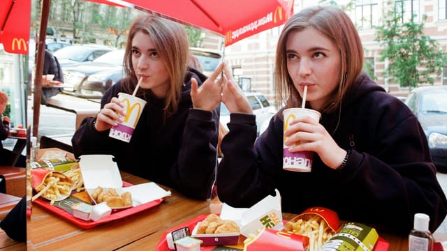 Young woman sipping soda at McDonald's with fries and nuggets.