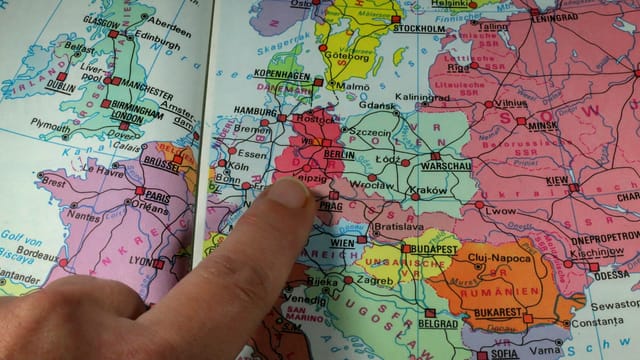 A finger points to Berlin on a colorful political map of Europe during the Cold War era.