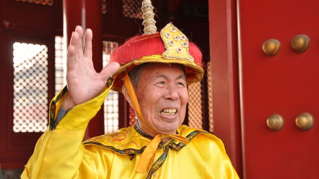 Elderly man in vibrant traditional attire smiling outdoors, showcasing cultural heritage.