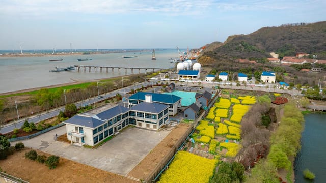 Stunning aerial shot of Jiujiang, China, featuring a river, yellow fields, and wind turbines.