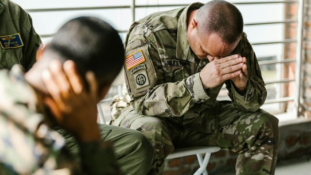 Two soldiers in military uniforms expressing emotions indoors, depicting stress and companionship.