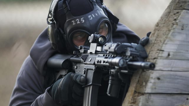 A tactical soldier in full gear aiming a rifle during an operation outdoors.