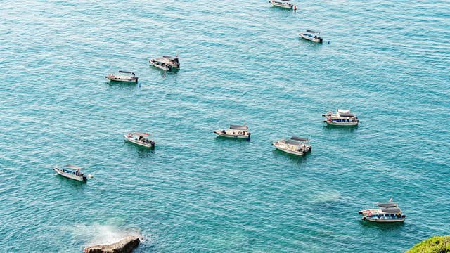 Aerial view of multiple boats floating on calm turquoise sea under bright daylight.