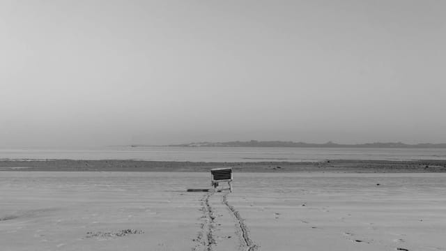 A solitary cart on an expansive beach seashore, captured in a tranquil black and white scene.