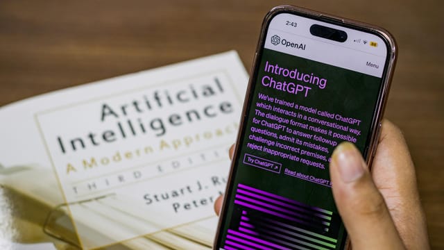 Close-up of a smartphone displaying ChatGPT app held over AI textbook.