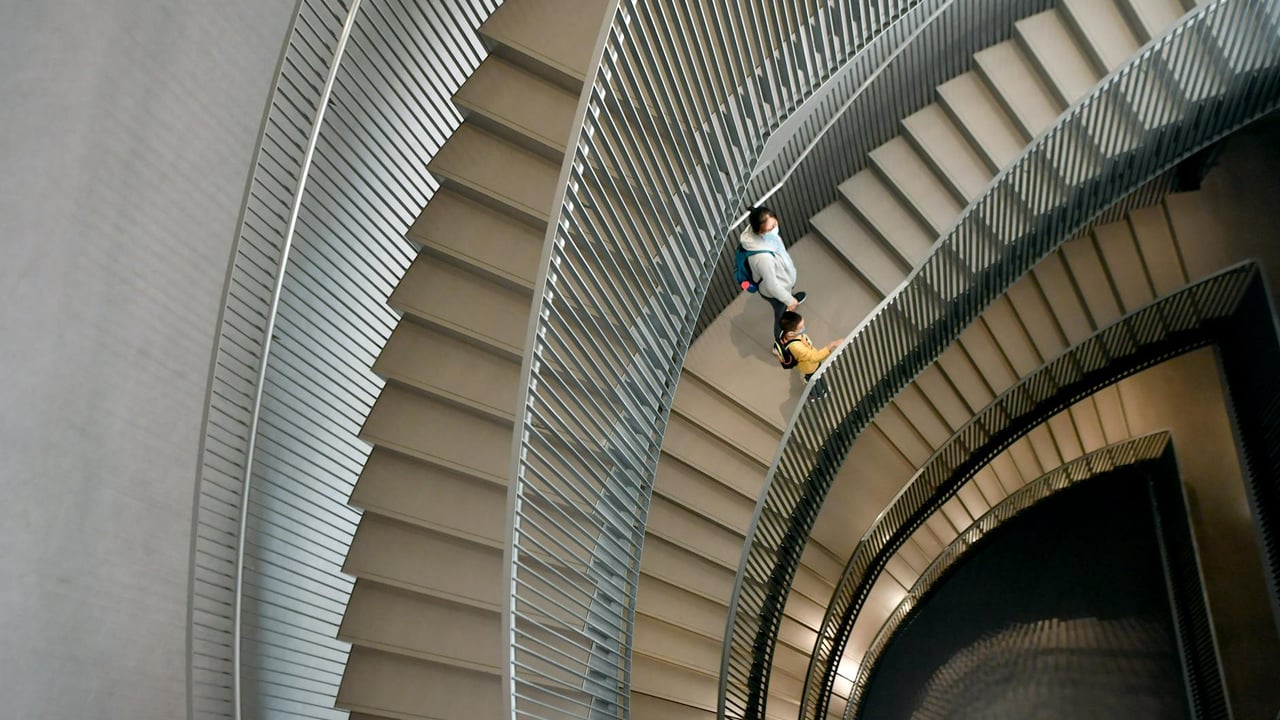 A woman walks down a spiral staircase in a modern building.