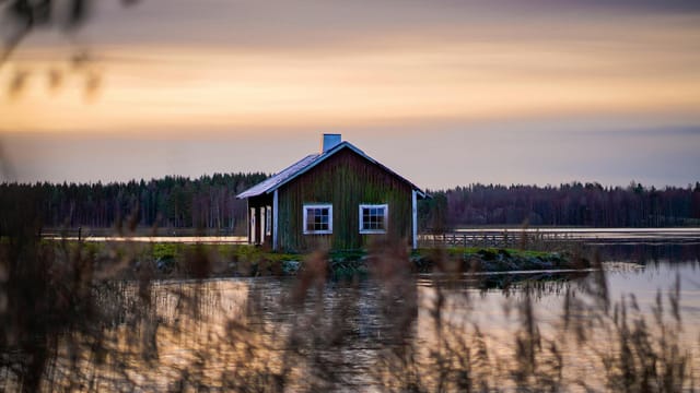Peaceful cabin on a serene lake during sunset, surrounded by nature's beauty and tranquil reflections.