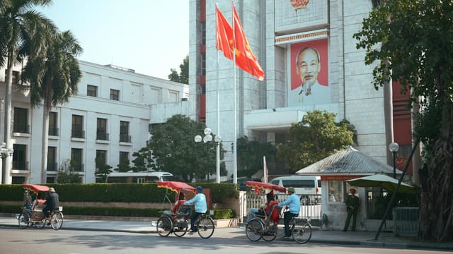 Cyclo riders passing by government building in Hanoi, Vietnam.