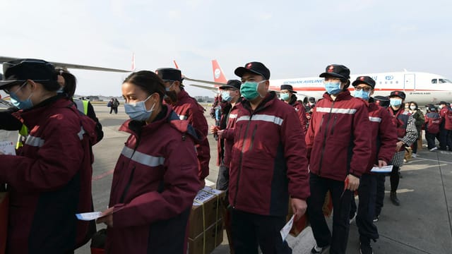 Masked workers in red jackets line up on airport tarmac in front of Sichuan Airlines plane.