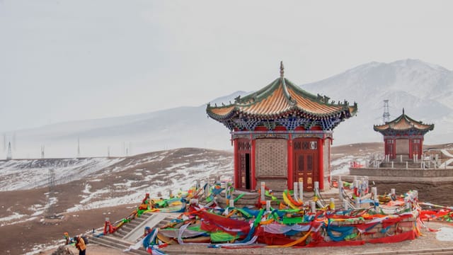 Vibrant Tibetan temple with prayer flags set against a snowy mountain backdrop, capturing winter serenity.