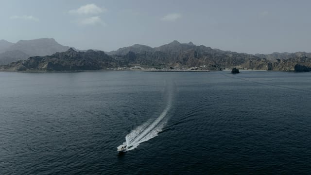 Aerial view of a boat navigating the waters near Muscat, Oman, with mountains in the background.