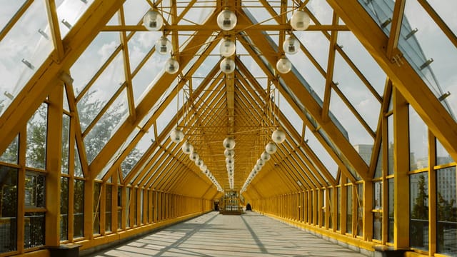 A spacious yellow steel truss footbridge with a glass ceiling, offering a bright pathway.