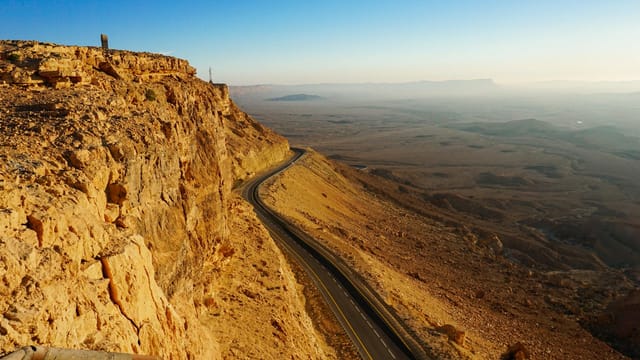 Explore the breathtaking arid landscape of the Mitzpe Ramon Crater with a winding road and expansive desert views.