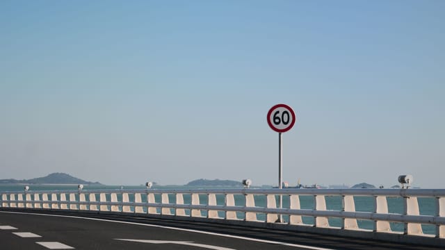 Calm coastal road on a bridge with a speed limit of 60 km/h and distant islands.