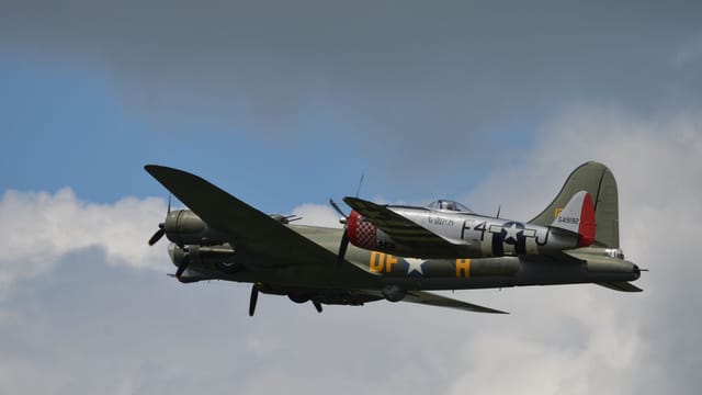 A historic World War II bomber aircraft captured mid-flight against a backdrop of clouds, showcasing classic military aviation.