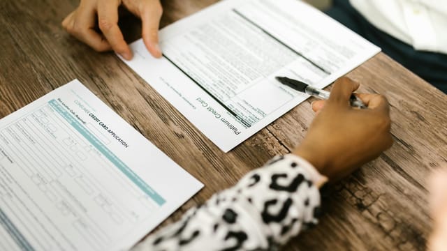 Close-up of two people reviewing and filling out a credit card application on a wooden table.