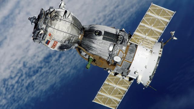 Close-up of Soyuz spacecraft orbiting Earth with solar panels extended, showcasing space exploration technology.