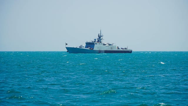 A navy patrol ship sailing on clear tropical waters under a bright sky.