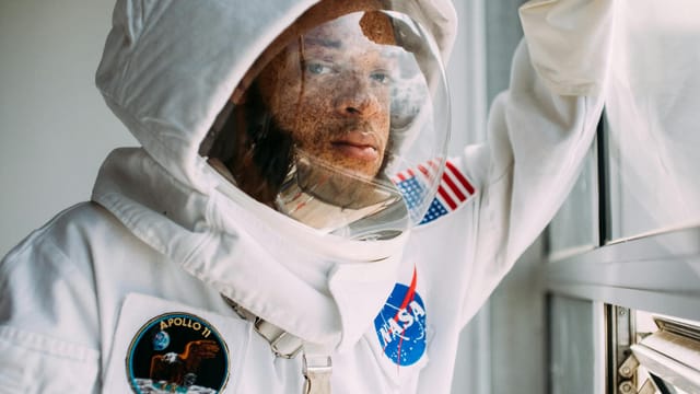 Close-up portrait of an astronaut wearing a NASA space suit looking out a window.