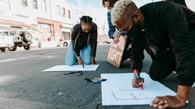 Protesters creating signs for a street demonstration in an urban area.
