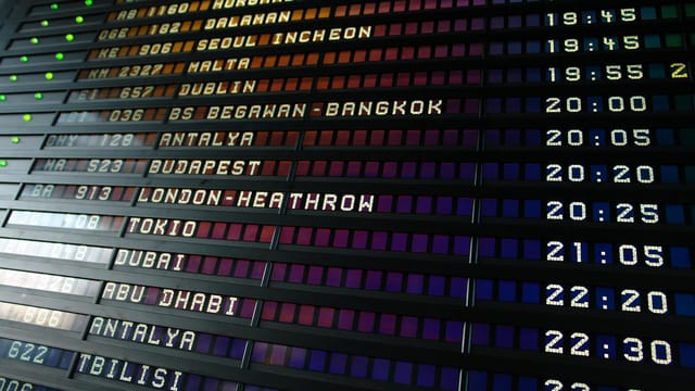 Retro flip-style airport departure board showing international flight destinations and times.