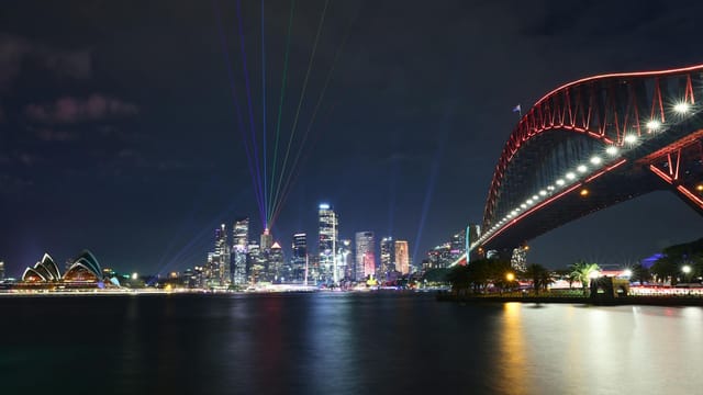 Vivid night view of Sydney Harbour featuring the illuminated Opera House, CBD skyline, and Harbour Bridge.