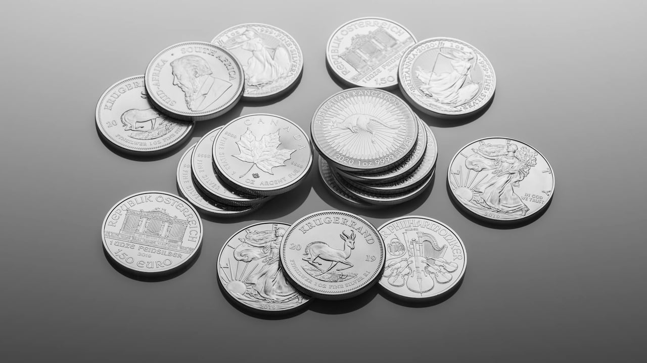 A close-up of various silver bullion coins, showcasing intricate designs on a reflective surface.