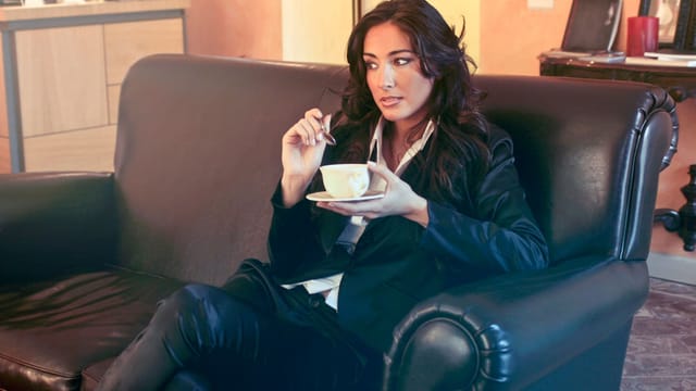 Stylish businesswoman enjoying a coffee break in a modern office lounge, conveying relaxation and elegance.