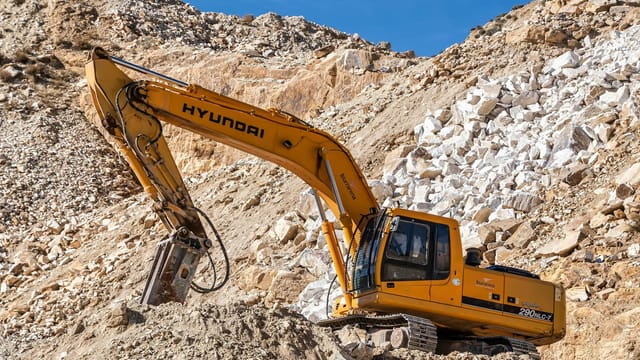 Yellow Hyundai excavator operating in a rocky quarry under a clear blue sky. Perfect for industrial themes.