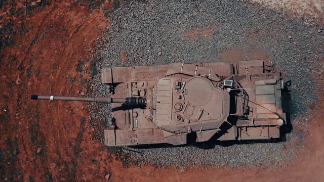Aerial shot of a military tank parked on rugged terrain captured by drone.