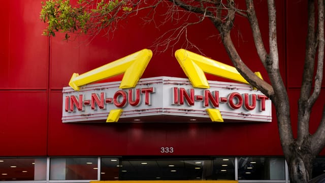 Iconic In-N-Out Burger sign with bold red background and trees in the foreground.