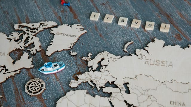 Wooden world map featuring a miniature boat, compass rose, and 'travel' tiles.