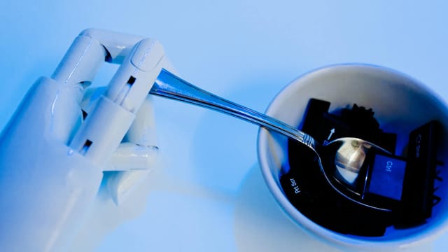 A robotic hand holding a spoon above a bowl with keyboard keys, showcasing technology themes.