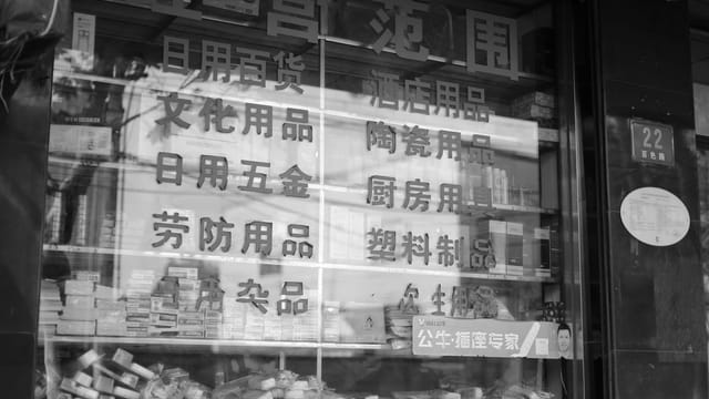 Black and white photo of a Chinese store window display showing various products and signage.