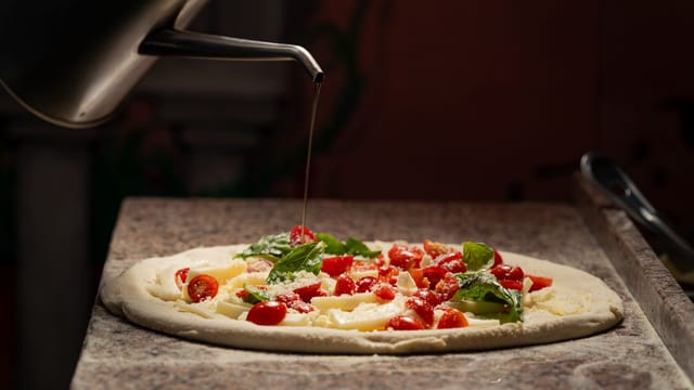 Delicious margherita pizza topped with fresh basil, mozzarella, and tomatoes being drizzled with olive oil.