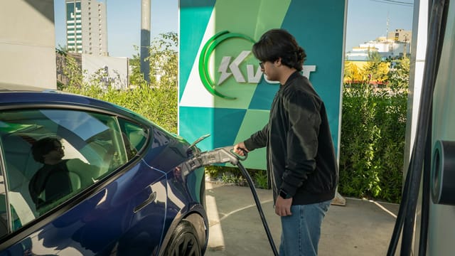 Young man charging a Tesla Model 3 at an outdoor electric vehicle station during the day.