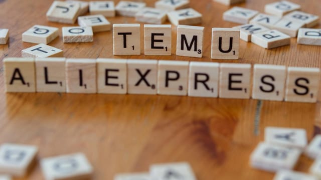 Close-up of Scrabble tiles on a wooden surface spelling 'TEMU' and 'ALIEXPRESS' amid scattered letters.