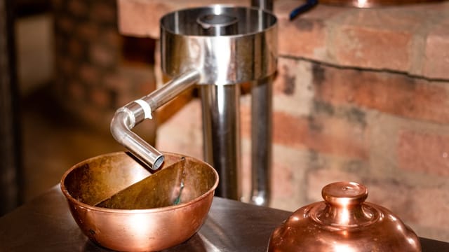 Close-up of copper distillation apparatus against a rustic brick background, indoors.