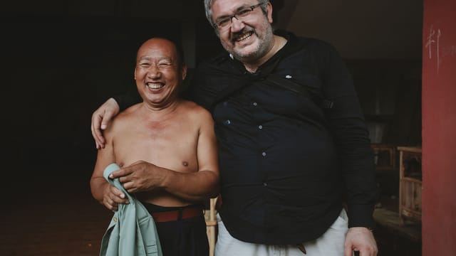 Two smiling men standing and embracing indoors, capturing a moment of friendship.