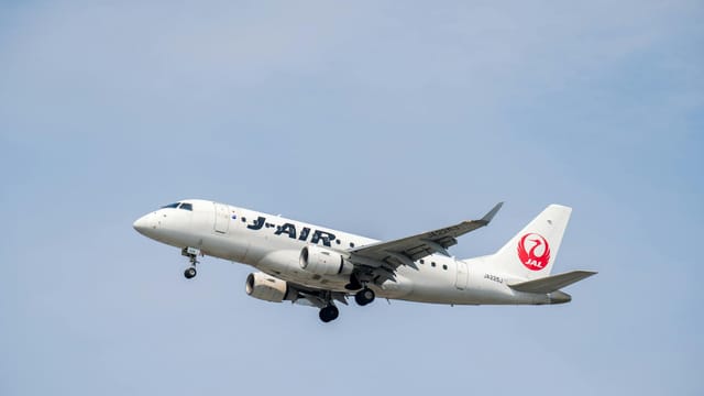A J-Air passenger plane flies high against a clear blue sky, capturing aviation travel moments.