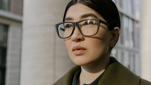 Close-up portrait of a confident woman in glasses, exuding professionalism in an urban environment.