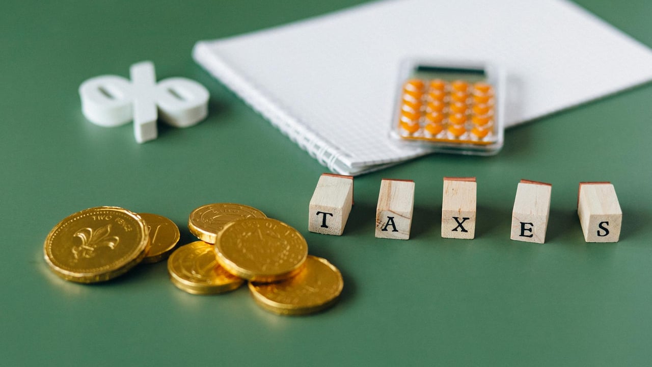 Close-up of tax-related items including coins, calculator, and word 'taxes' on a green background.
