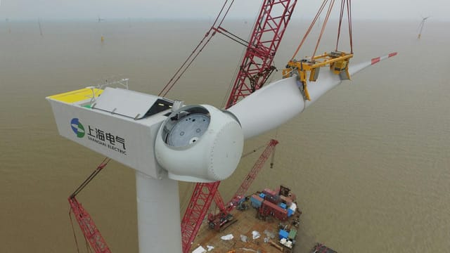 Aerial view of a wind turbine being installed over the sea, showcasing renewable energy construction.