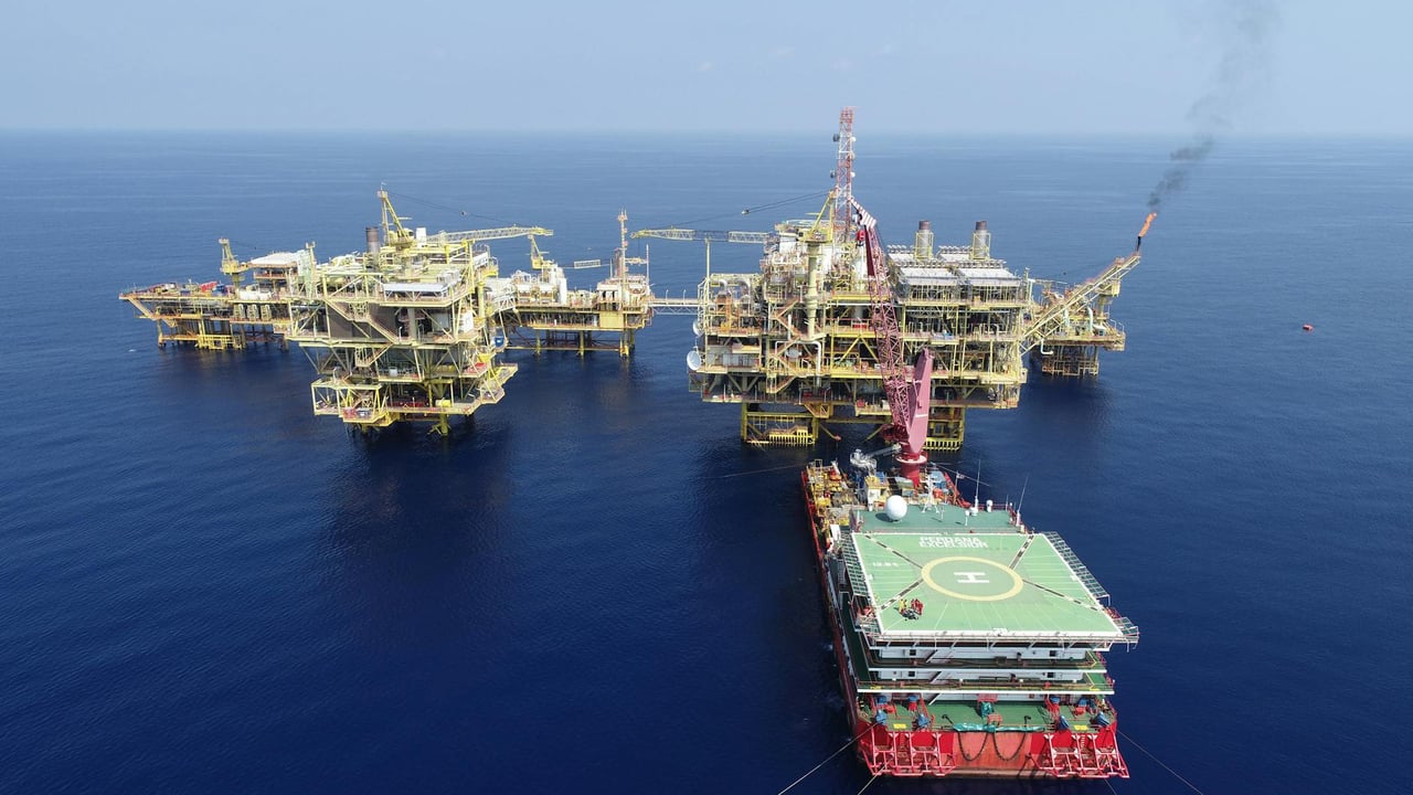 Aerial shot of multiple offshore oil platforms in a serene, blue sea under clear skies.