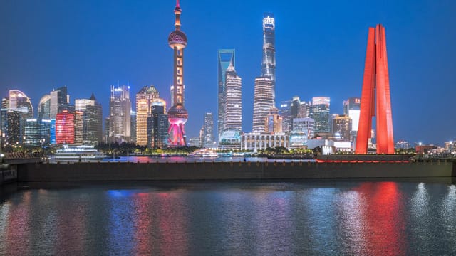 Explore the vibrant Shanghai skyline lit up at night, featuring iconic buildings and reflections on the river.