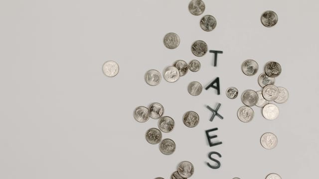 Scattered coins forming the word 'TAXES' on a white surface, symbolizing financial concepts.