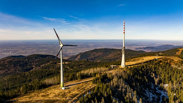 Scenic aerial view of a hillside with a wind turbine and broadcast tower under a clear sky.